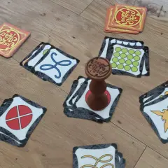 Karty do gry Jungle Speed leżą na drewnianej podłodze. Widać totem i różne symbole na kartach.