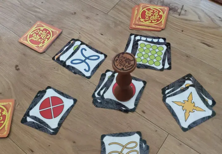 Karty do gry Jungle Speed leżą na drewnianej podłodze. Widać totem i różne symbole na kartach.