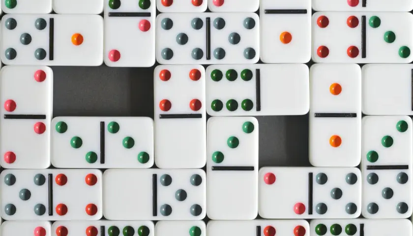 Wiele białych kostek do gry w domino z kolorowymi kropkami, ułożonych w rzędach. To klasyczna domino gra.