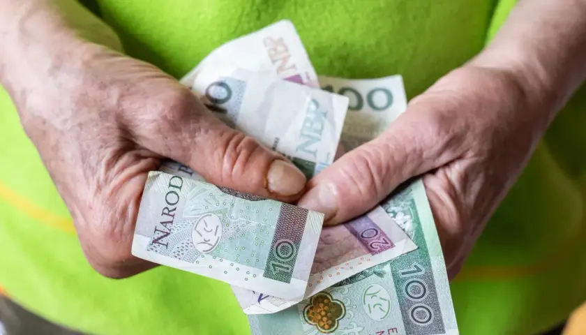 Dłonie trzymają polskie banknoty: 10, 20 i 100 zł. Ile pieniędzy na start w grze Monopoly?