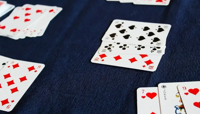 Karciana gra z dżokerami w toku. Na granatowym tle leżą karty: dziesiątki pik, karo i trefl, a także dziewiątki i siódemki kier.