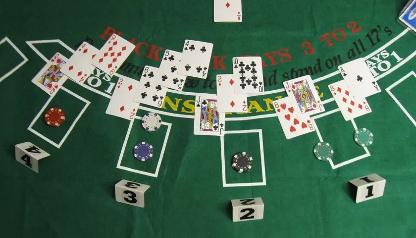 Kier karty na zielonym stole do blackjacka. Widoczne karty, żetony i kostki z numerami.